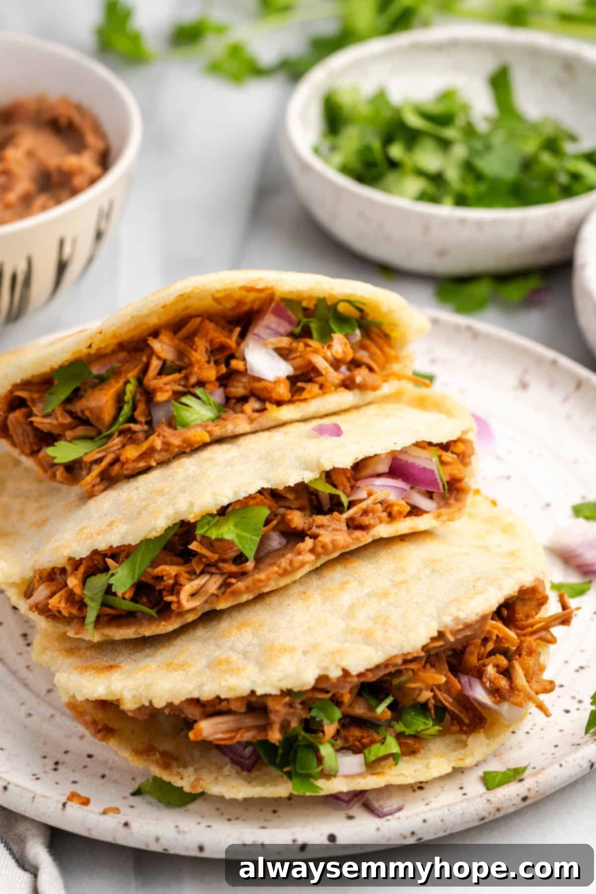 Three golden brown homemade vegan jackfruit gorditas piled on a white plate, garnished with fresh cilantro and lime wedges, ready to be served.