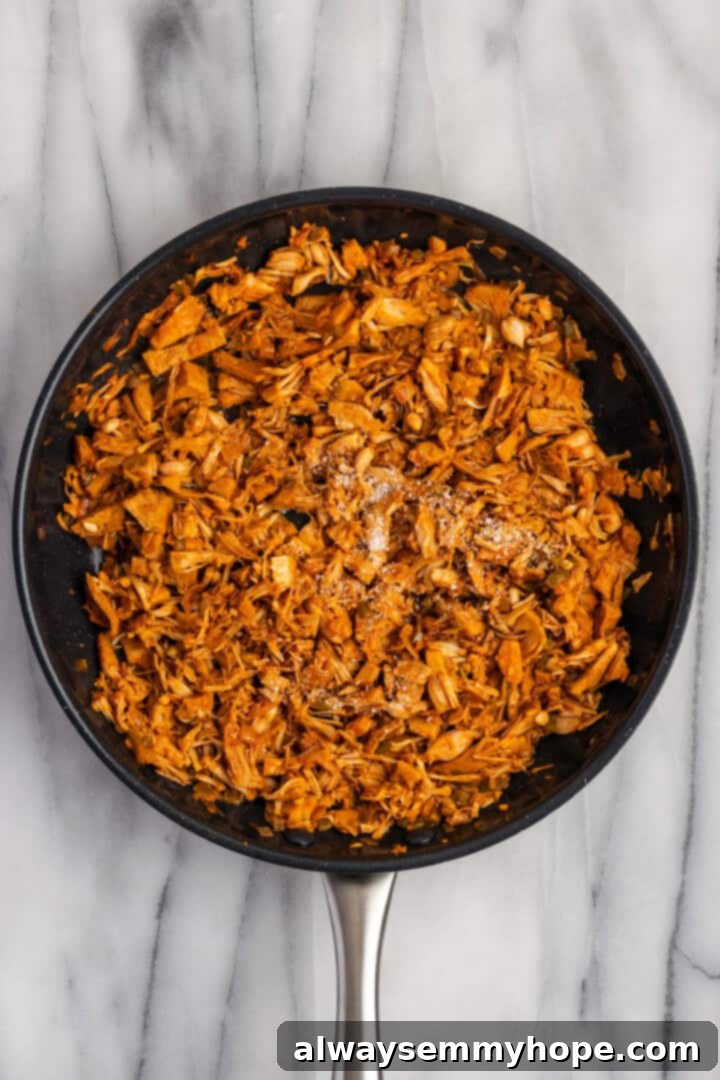 Overhead view of shredded jackfruit cooking in a skillet, appearing dried out and beginning to crisp, mixed with maple syrup and salt for a sweet and savory finish.