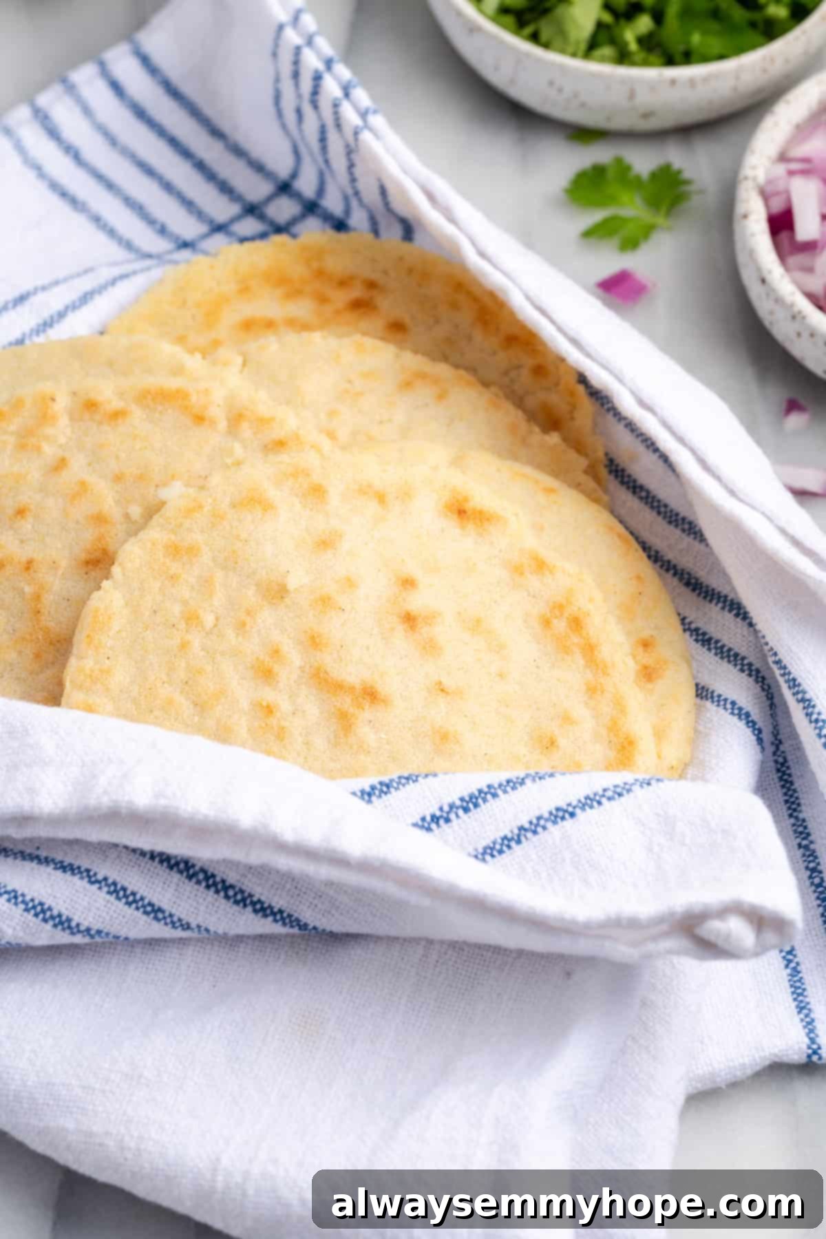 A stack of freshly cooked homemade gorditas, covered with a clean white kitchen towel to keep them warm and soft until serving.