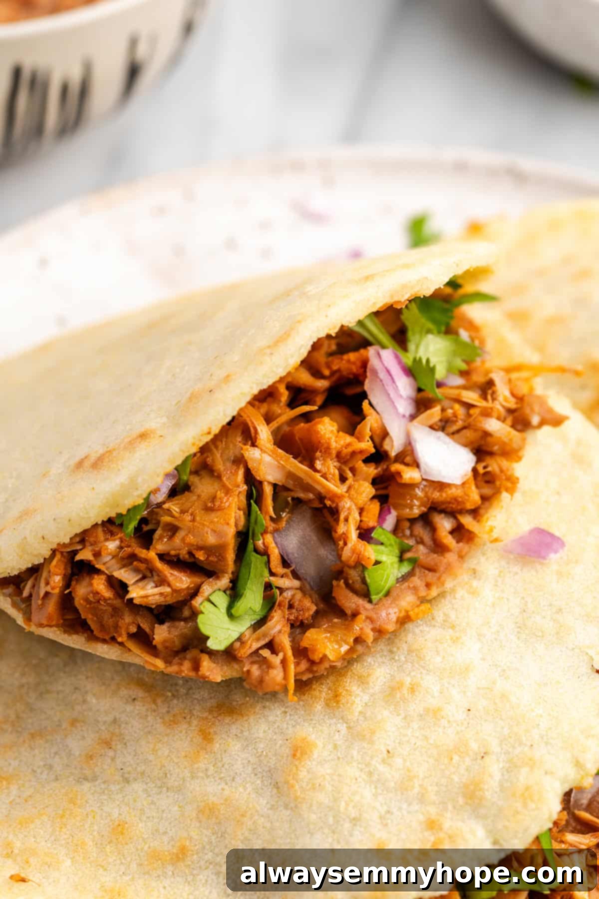 Three golden homemade gorditas stacked on a plate, with one cut open revealing the rich, flavorful vegan jackfruit filling inside, ready to be enjoyed.