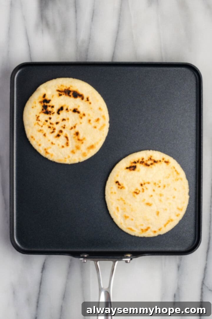 Overhead view of several gorditas cooking and puffing up on a hot cast iron skillet or comal, showing golden brown spots.