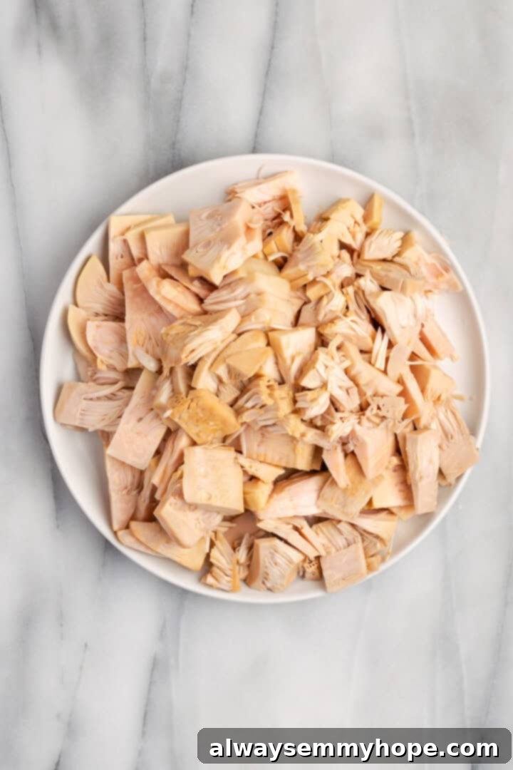 Overhead view of canned young jackfruit, drained and sliced into small pieces, ready for cooking, on a white plate.