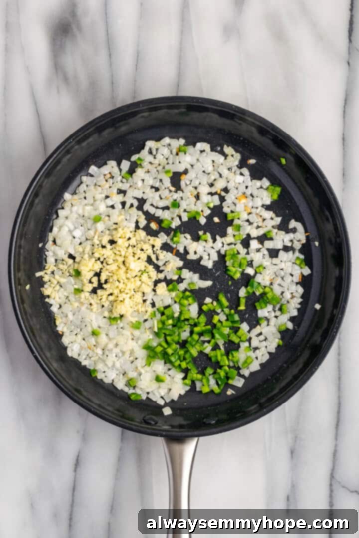 Overhead view of diced onions, minced garlic, and sliced jalapeño sautéing in olive oil in a hot skillet, releasing aromatic flavors.
