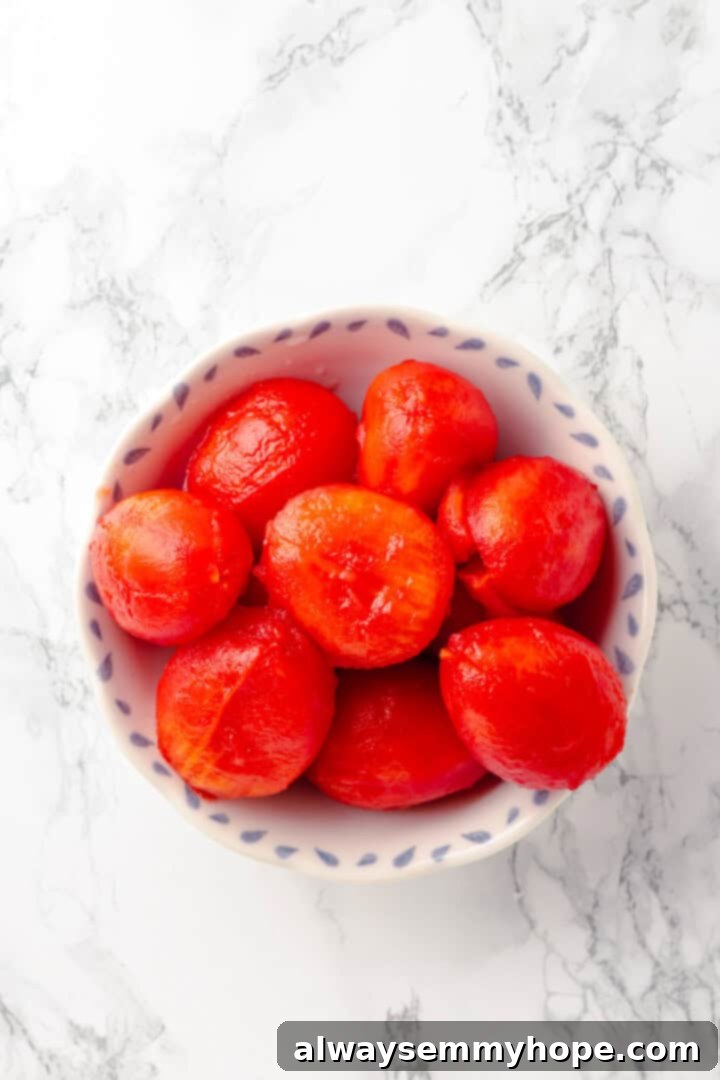 This homemade pomodoro sauce recipe takes a short list of simple ingredients and transforms them into a fresh, vibrant pasta sauce. So easy! Overhead view of blanched Roma tomatoes in a bowl, ready for peeling, showing the scored 'X' mark.