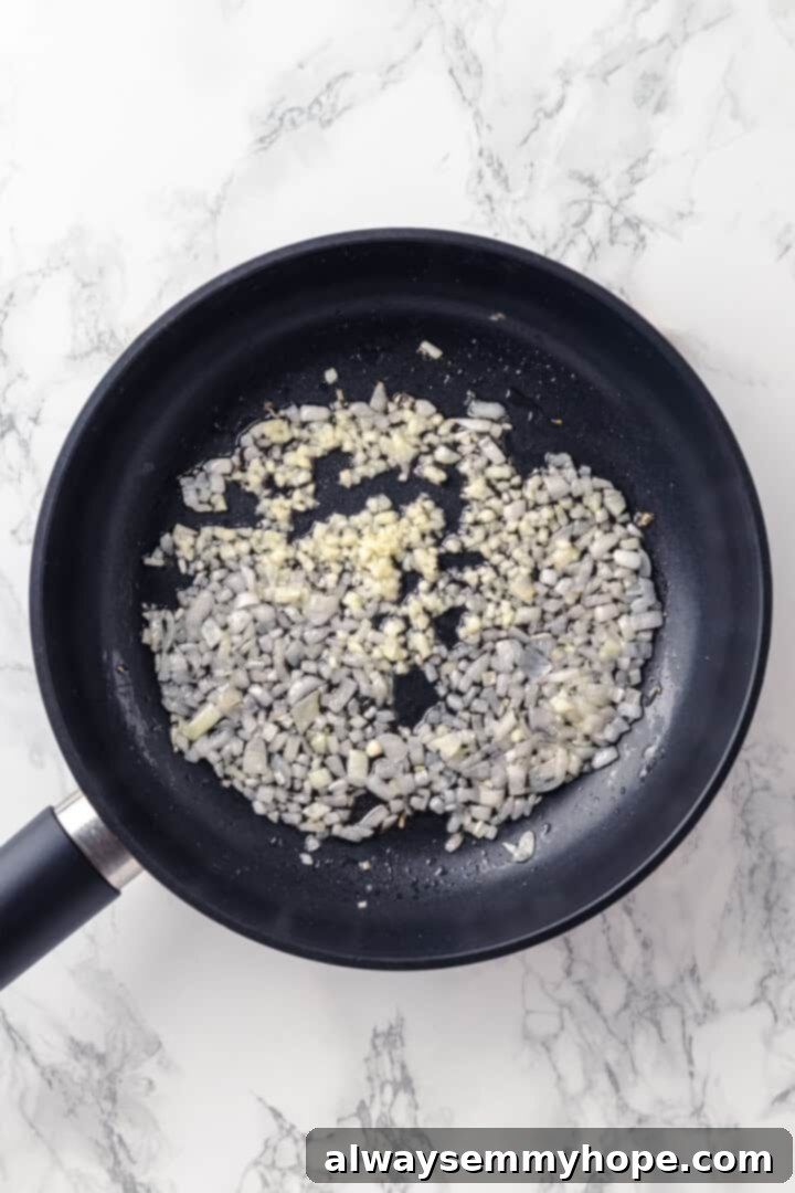 This homemade pomodoro sauce recipe takes a short list of simple ingredients and transforms them into a fresh, vibrant pasta sauce. So easy! Overhead view of finely chopped onions and minced garlic cooking gently in olive oil in a skillet.
