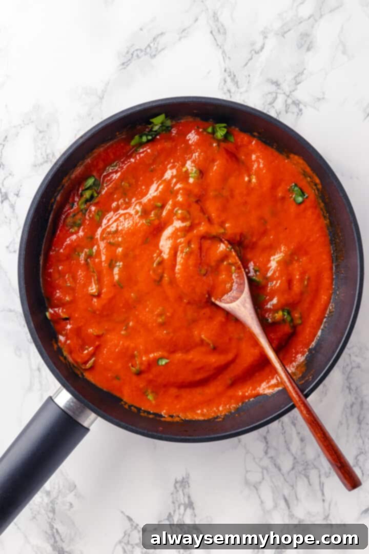 This homemade pomodoro sauce recipe takes a short list of simple ingredients and transforms them into a fresh, vibrant pasta sauce. So easy! Overhead view of pomodoro sauce in a skillet, after pureeing, with fresh basil being stirred in by a wooden spoon.