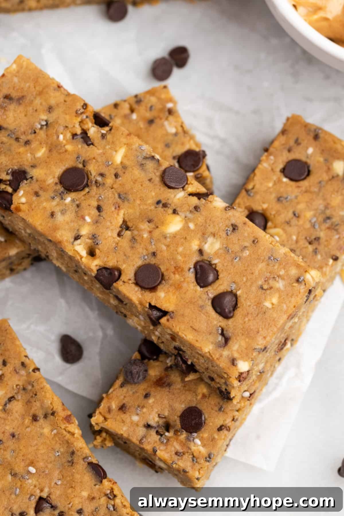 These homemade vegan protein bars are an easy, no-bake recipe that you can customise with your favourite flavours and mix-ins. So tasty! Closeup of homemade chocolate chip protein bars stacked on countertop with ingredients blurred in background
