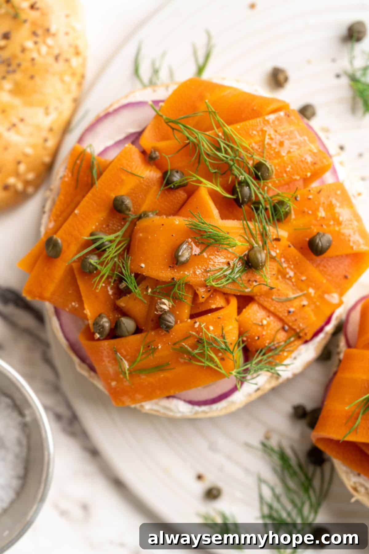 Overhead view of vegan carrot lox on a toasted bagel with cream cheese and fresh dill, ready to be eaten.