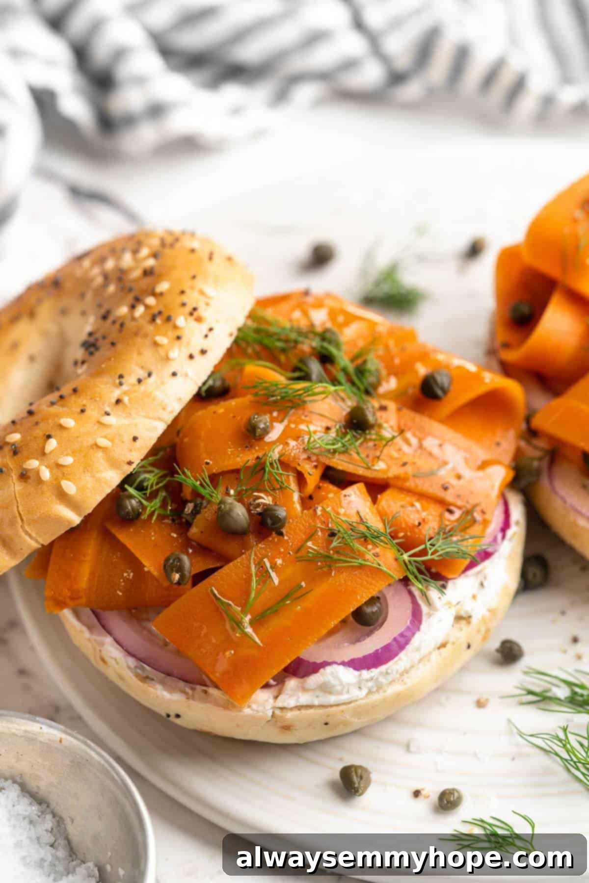 Close-up of a perfectly toasted bagel generously topped with creamy vegan cream cheese and vibrant homemade carrot lox, garnished with fresh dill.