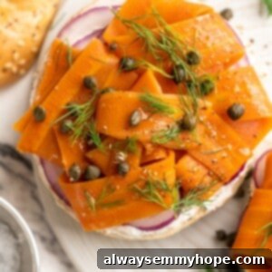 Overhead view of vegan carrot lox on a bagel with cream cheese, garnished with dill and capers.