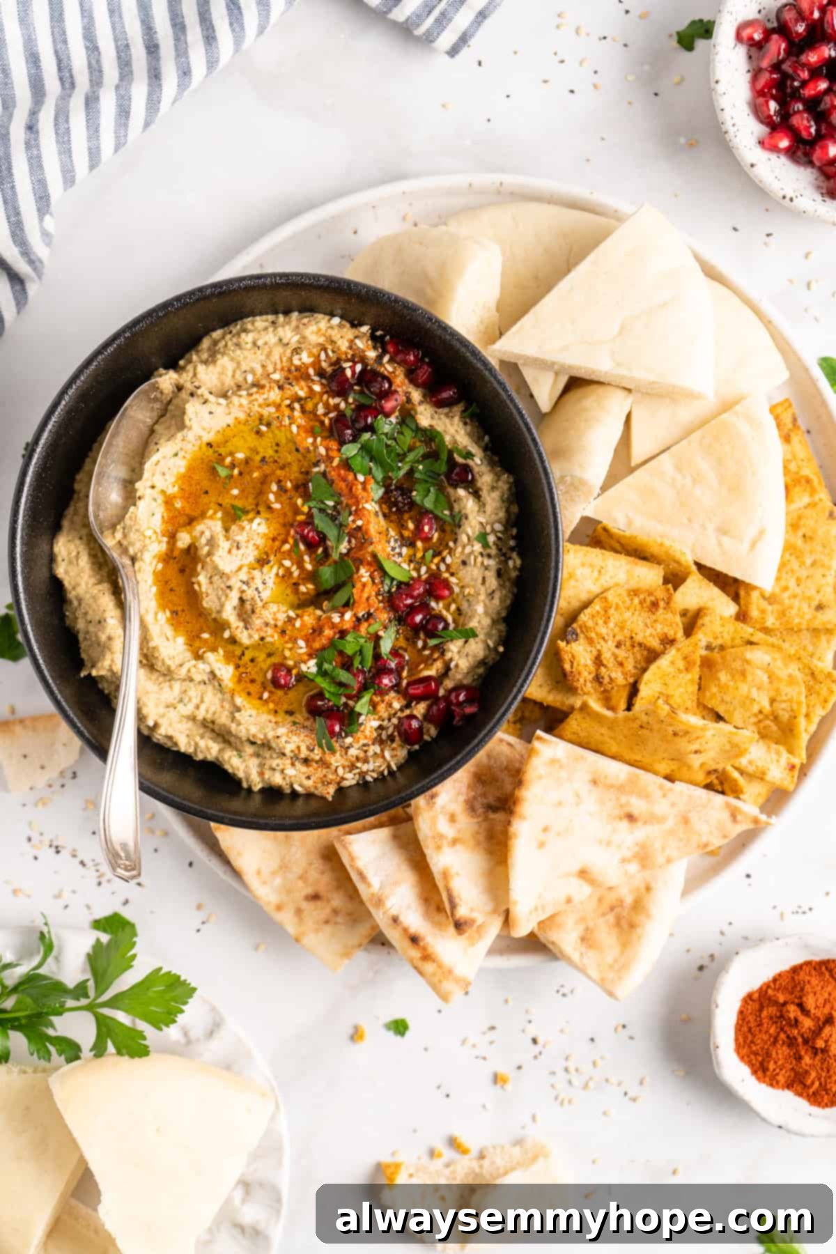 Overhead view of baba ghanoush in black bowl with spoon, surrounded by pitas on plate, ready to be served