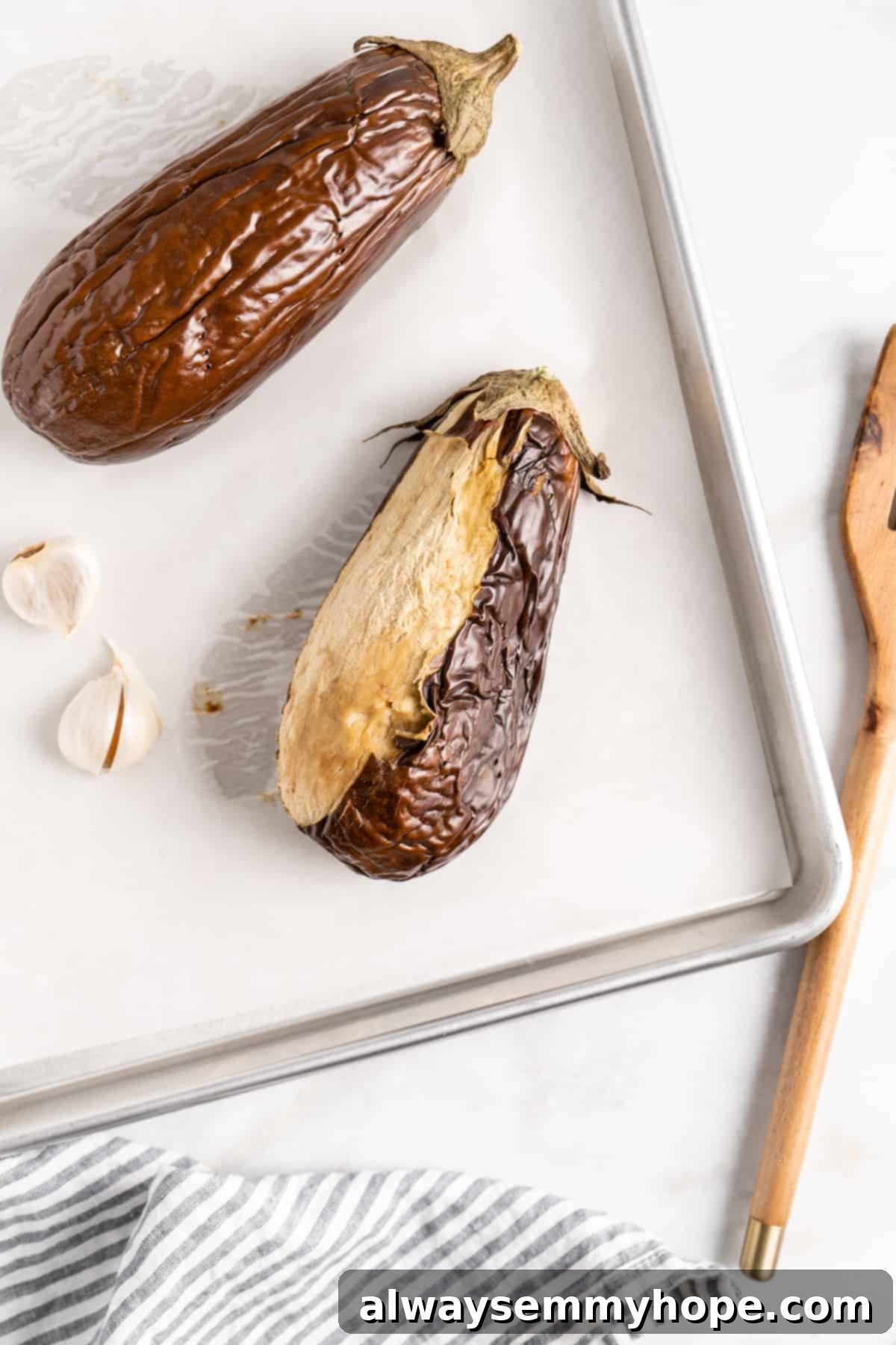 Roasted eggplants on baking sheet, with one half peeled, showing tender flesh