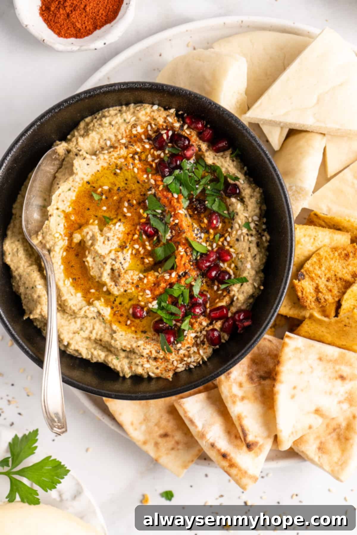 Overhead view of baba ghanoush in black bowl with spoon, surrounded by pitas
