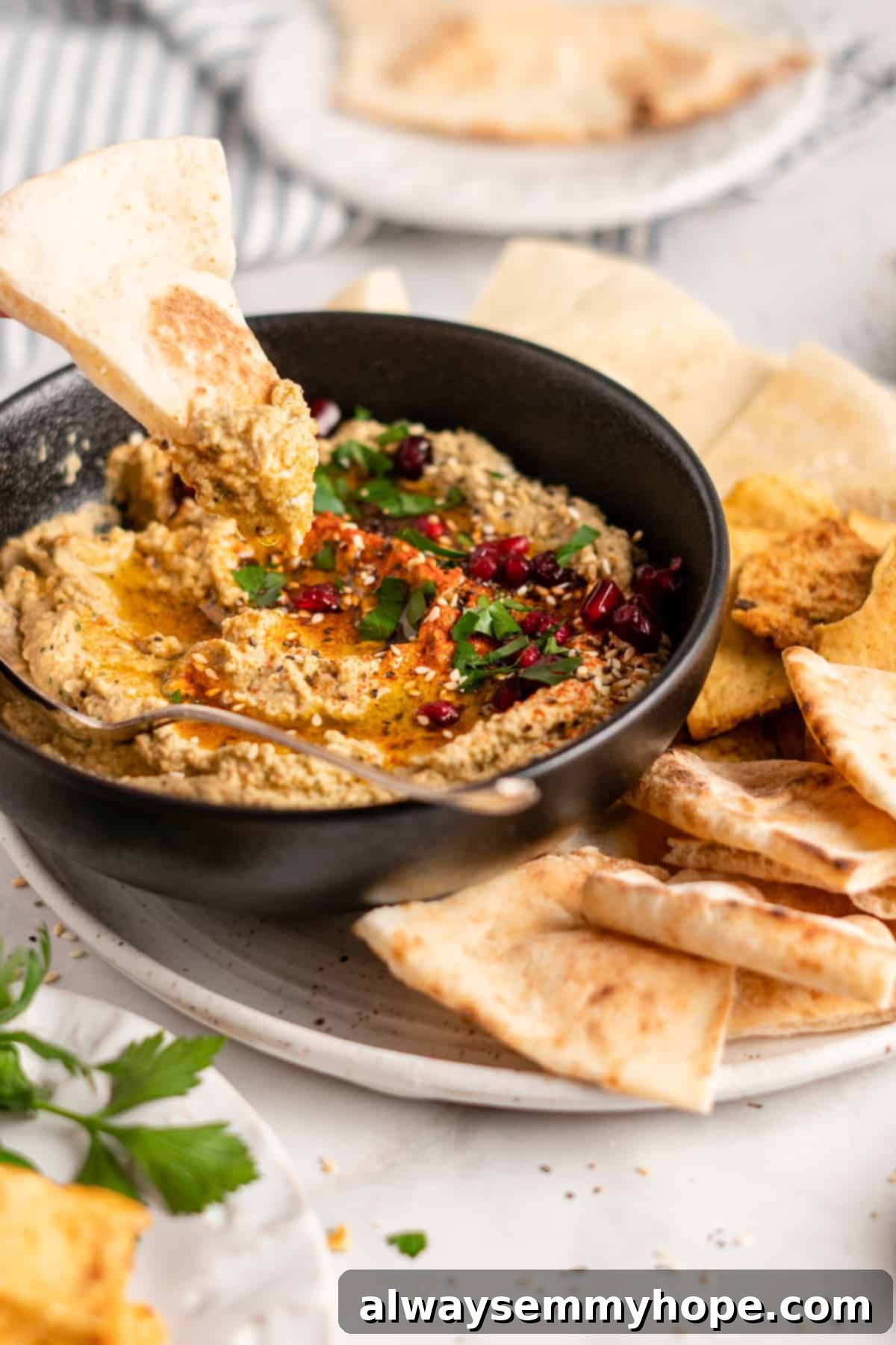 Baba ghanoush in bowl surrounded by triangles of pita on plate, garnished with olive oil and parsley