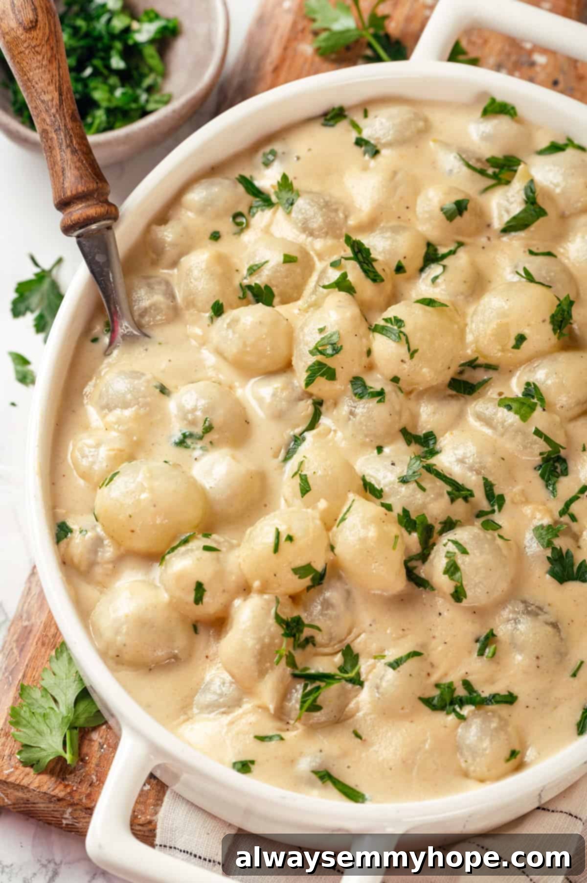 These creamed onions are sweet, savoury, and rich. A stovetop recipe perfect for holiday dinners but easy enough for a weeknight! Overhead view of creamed onions in dish with spoon