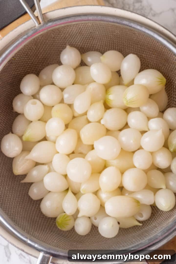 These creamed onions are sweet, savoury, and rich. A stovetop recipe perfect for holiday dinners but easy enough for a weeknight! Overhead view of pearl onions in sieve