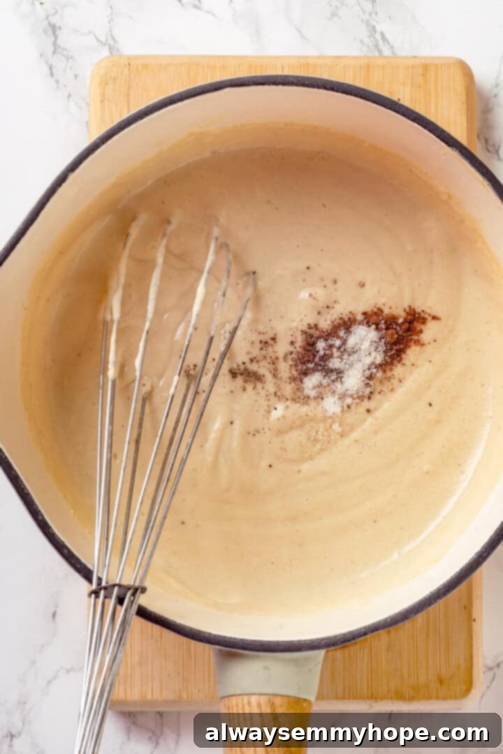 These creamed onions are sweet, savoury, and rich. A stovetop recipe perfect for holiday dinners but easy enough for a weeknight! Overhead view of sauce for creamed onions in pot with whisk