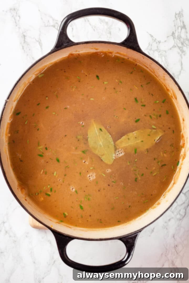 This vegan French onion soup recipe is full of rich, savoury flavour, and lots of melty cheese! The perfect cozy dinner for a chilly day. Overhead view of French onion soup in Dutch oven with bay leaves