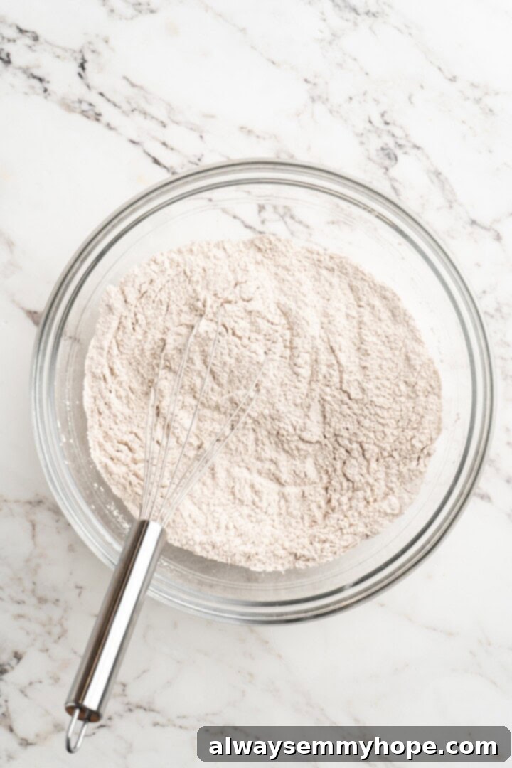 Vegan pumpkin bread with cream cheese frosting is moist, full of cozy spices and the frosting takes it over the top. So easy to make too! Close-up of a glass bowl containing all-purpose flour, baking powder, baking soda, sea salt, cinnamon, and pumpkin pie spice, being whisked together vigorously.