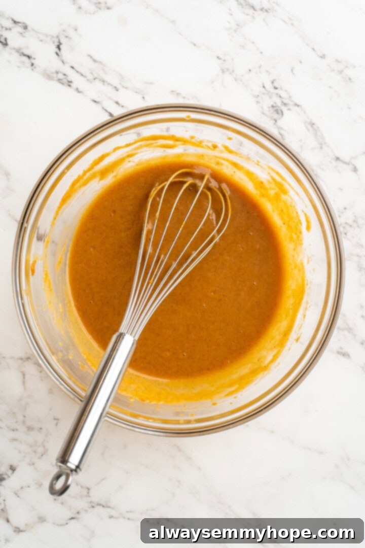 Vegan pumpkin bread with cream cheese frosting is moist, full of cozy spices and the frosting takes it over the top. So easy to make too! Overhead view of a bowl filled with pumpkin puree, brown sugar, oil, vegan milk, and vanilla extract, being mixed with a whisk to combine all wet ingredients.