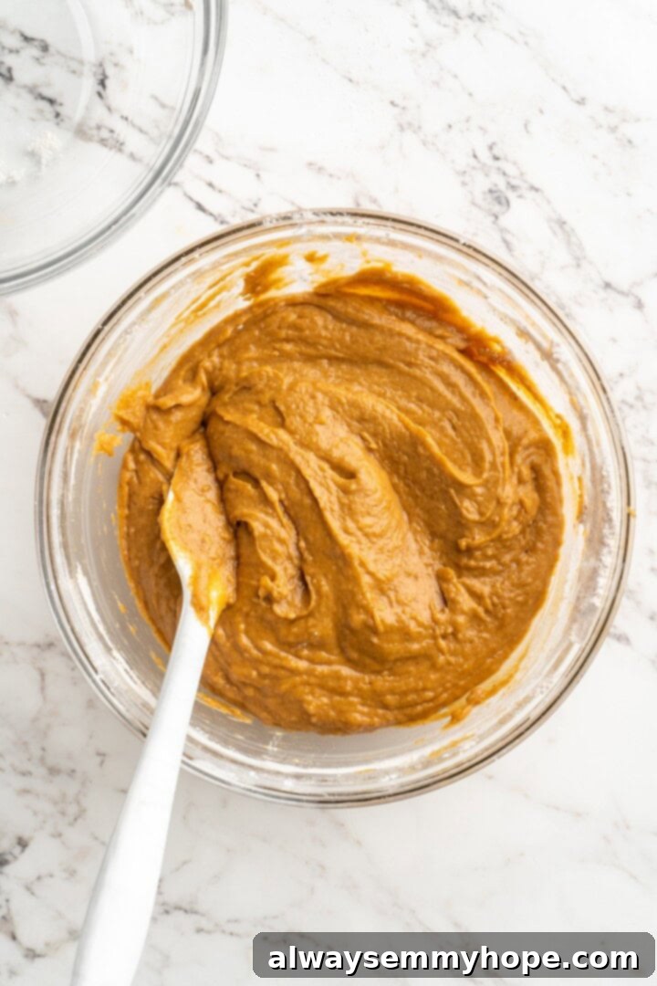 Vegan pumpkin bread with cream cheese frosting is moist, full of cozy spices and the frosting takes it over the top. So easy to make too! Overhead shot of a bowl containing a thick, smooth orange pumpkin bread batter, ready for baking.
