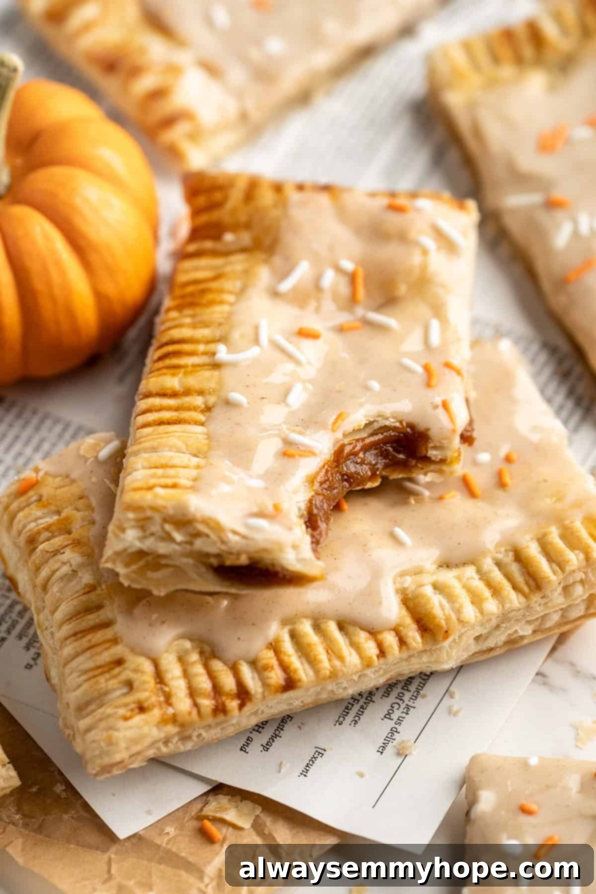 A cozy pumpkin-spiced filling is tucked into flaky vegan puff pastry to make these easy and delicious homemade pumpkin pop tarts! Two homemade vegan pumpkin pop tarts stacked on top of each other, with one bitten in corner revealing the pumpkin filling