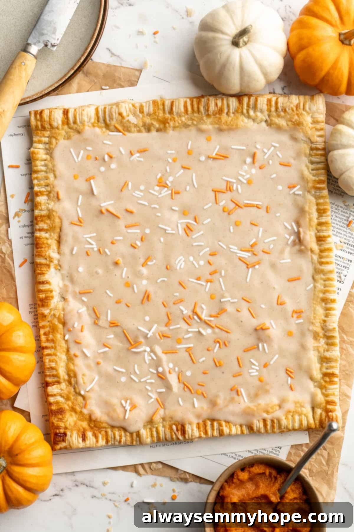 A cozy pumpkin-spiced filling is tucked into flaky vegan puff pastry to make these easy and delicious homemade pumpkin pop tarts! Overhead view of a single large frosted vegan pumpkin pop tart before it's cut into individual servings.