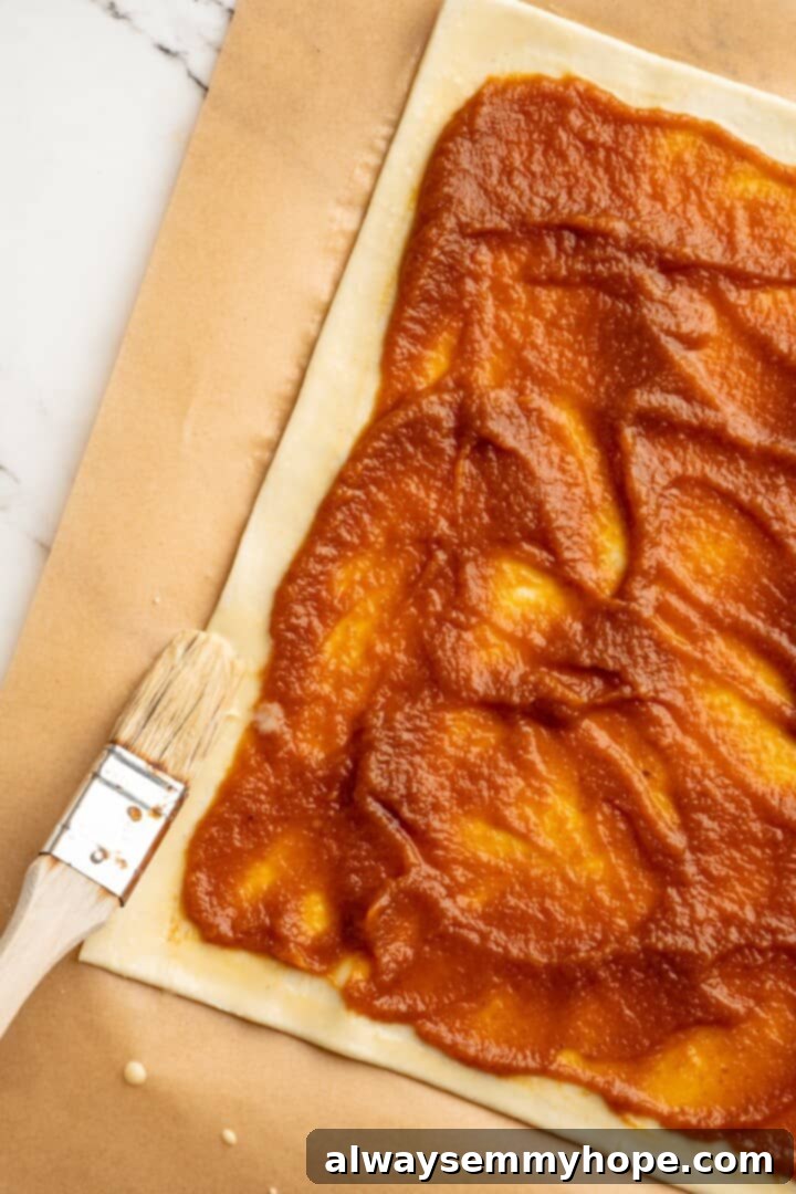 A cozy pumpkin-spiced filling is tucked into flaky vegan puff pastry to make these easy and delicious homemade pumpkin pop tarts! Brushing vegan egg wash onto the edges of a puff pastry sheet after adding pumpkin filling.