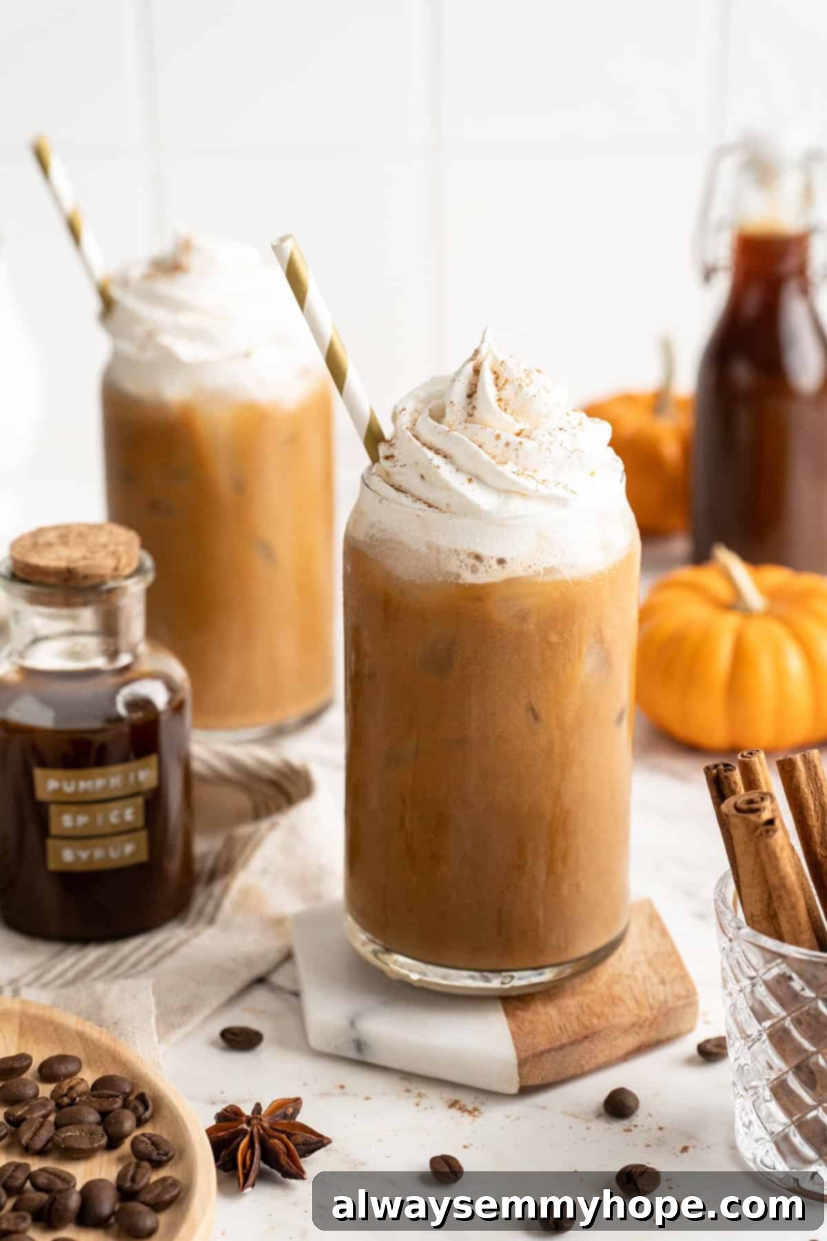 This vegan pumpkin spice latte recipe is a homemade version of the coffee house favourite. It's just as cozy and delicious as the original! Two pumpkin spice lattes with vegan whipped cream, garnished with pumpkin pie spice, on a rustic wooden surface, perfect for a cozy autumn day.