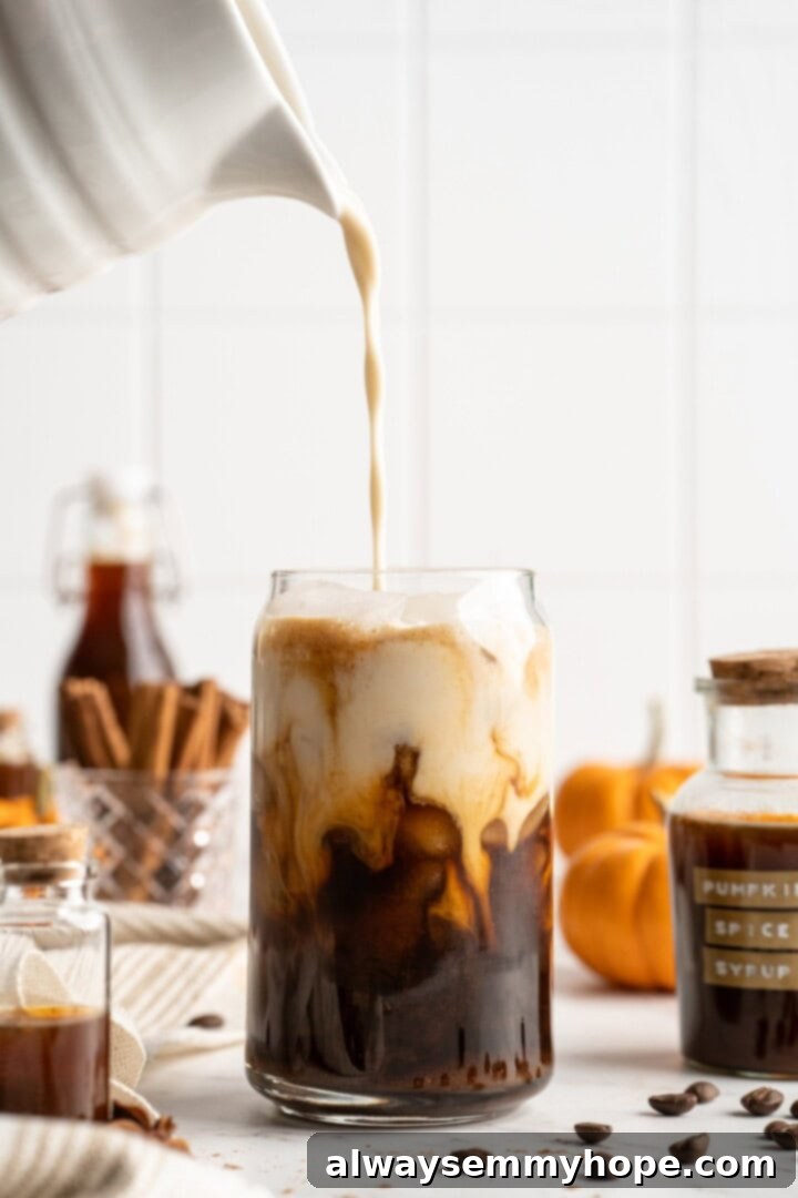 This vegan pumpkin spice latte recipe is a homemade version of the coffee house favourite. It's just as cozy and delicious as the original! Pouring vegan plant-based milk over ice and espresso-syrup mixture for an iced pumpkin spice latte.