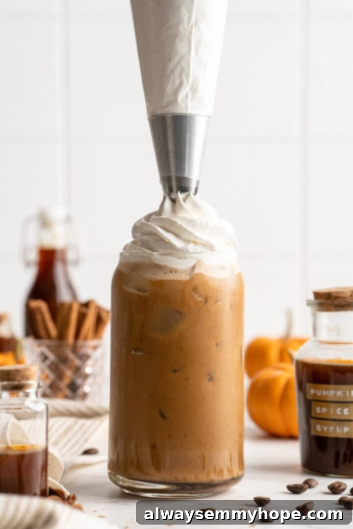 This vegan pumpkin spice latte recipe is a homemade version of the coffee house favourite. It's just as cozy and delicious as the original! Adding a generous dollop of vegan whipped cream to a finished pumpkin spice latte, ready for garnish.