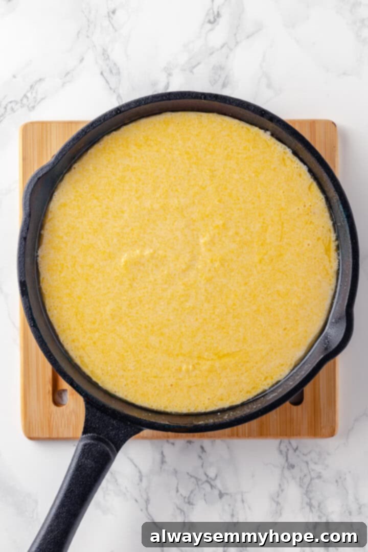 This vegan corn pone is crispy on the outside, tender on the inside, and so delicious! If you like cornbread, you’ll love this recipe. Corn pone batter being poured into a hot, greased cast iron skillet
