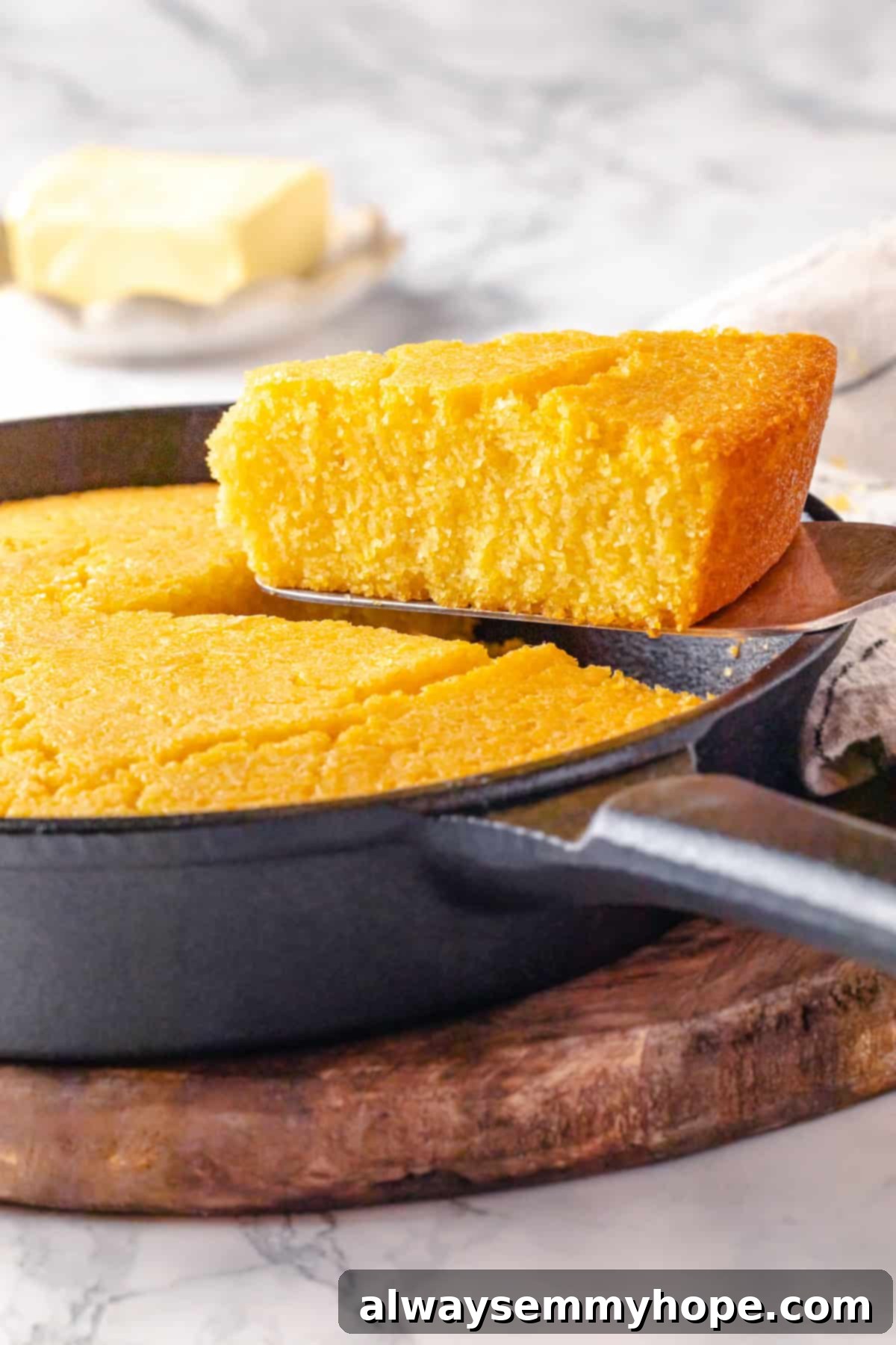 This vegan corn pone is crispy on the outside, tender on the inside, and so delicious! If you like cornbread, you’ll love this recipe. Spatula lifting a slice of crispy vegan corn pone from a cast iron skillet