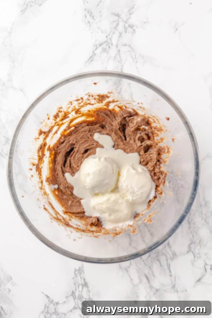 Integrating softened vegan ice cream into the butter base for a smoother consistency. Overhead view of softened vegan vanilla ice cream being added to the spiced butter mixture in a mixing bowl for the hot buttered rum base.