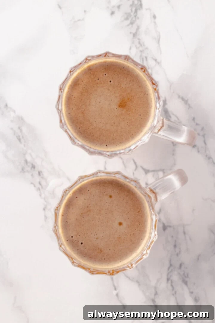 Finishing the hot buttered rum by adding hot water and stirring until combined. Overhead shot of vegan hot buttered rum in mugs, with hot water being poured over the butter base and rum, ready for stirring.