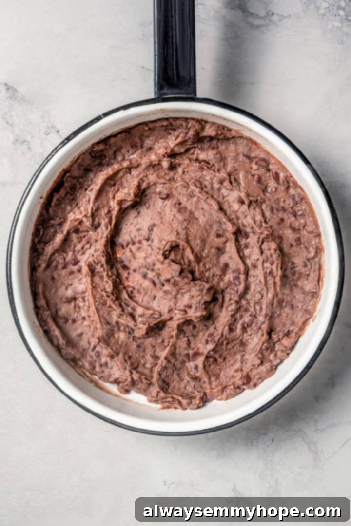 Easy tlacoyos filled with black beans. Top this homemade and vegan spin on Mexican street food with diced avocado, salsa and vegan cheese. Refried beans in a pot.