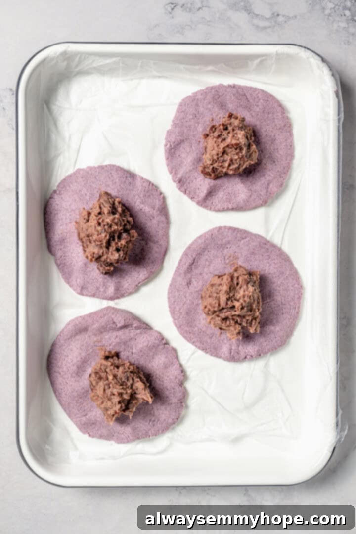 Easy tlacoyos filled with black beans. Top this homemade and vegan spin on Mexican street food with diced avocado, salsa and vegan cheese. Adding bean filling to flattened masa dough.