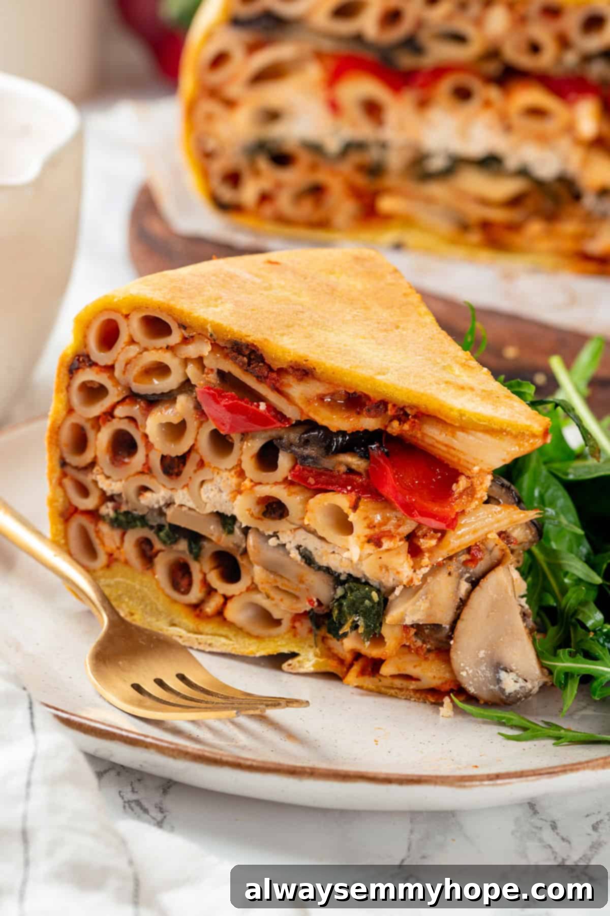 This vegan timpano recipe is perfect for the holidays! It’s loaded with pasta, veggies and plant-based cheese, all baked in a pastry crust. Closeup of a perfectly sliced vegan timpano, showcasing its vibrant layers of pasta, vegetables, and creamy vegan ricotta inside a golden pastry crust, resting on a white plate, ready to be enjoyed.