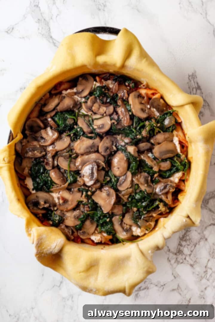 This vegan timpano recipe is perfect for the holidays! It’s loaded with pasta, veggies and plant-based cheese, all baked in a pastry crust. A vibrant layer of sautéed mushrooms, onions, and spinach spread over the pasta and cheese in the timpano, continuing the meticulous layering process.