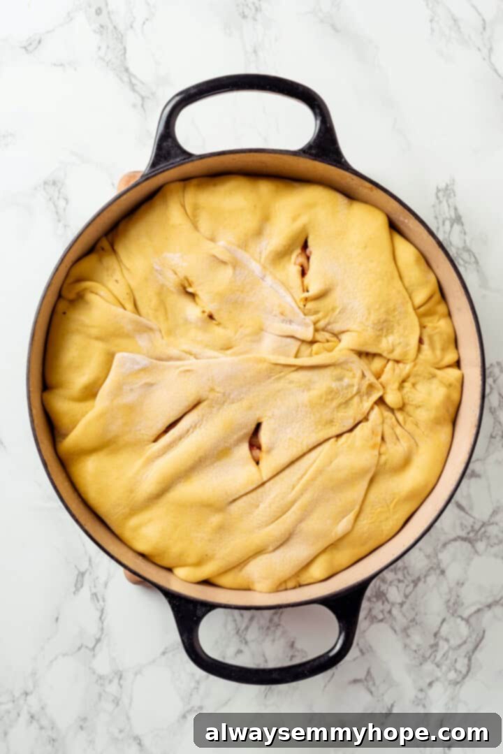 This vegan timpano recipe is perfect for the holidays! It’s loaded with pasta, veggies and plant-based cheese, all baked in a pastry crust. Overhead view of the assembled vegan timpano in a Dutch oven, with the dough folded over the filling and slits cut into the top for venting, ready for baking.