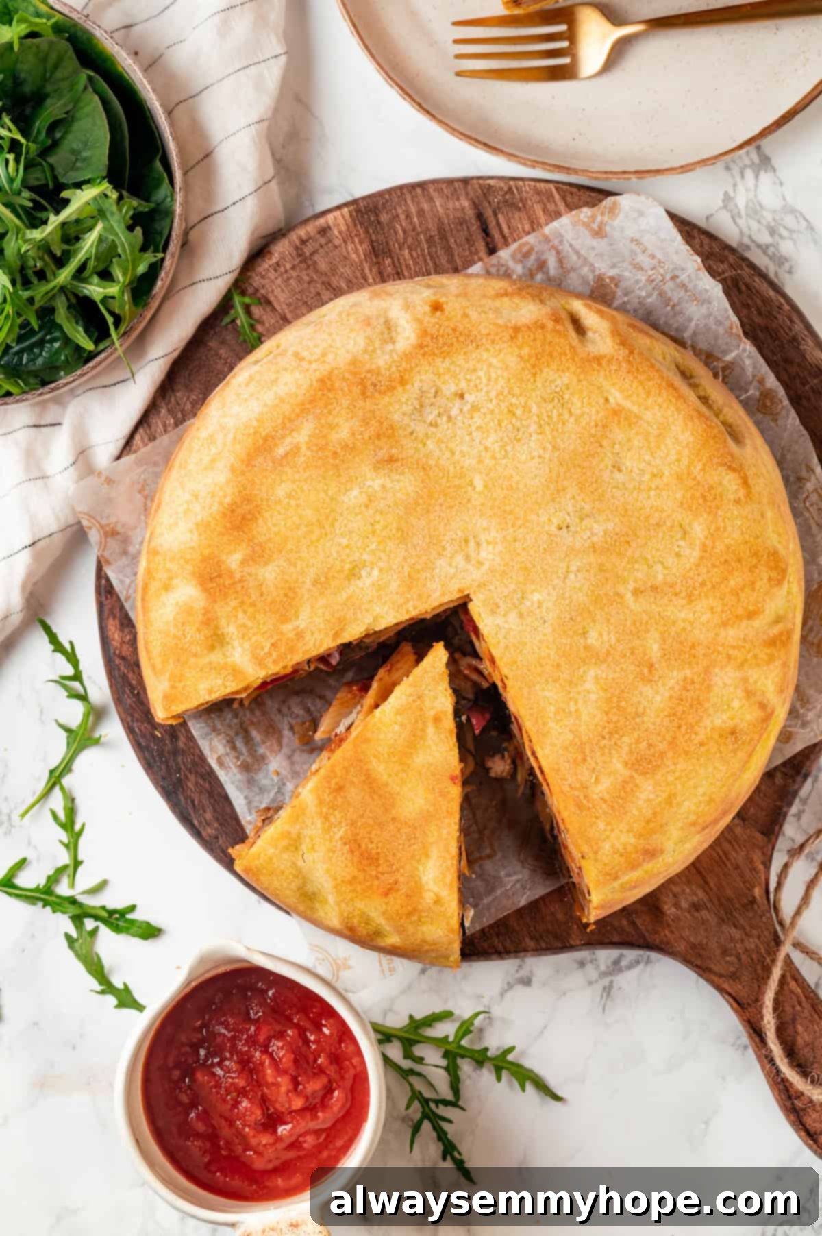 This vegan timpano recipe is perfect for the holidays! It’s loaded with pasta, veggies and plant-based cheese, all baked in a pastry crust. Overhead view of the whole vegan timpano, freshly baked with a golden crust, with one slice elegantly removed, revealing its intricate and colorful layers inside.