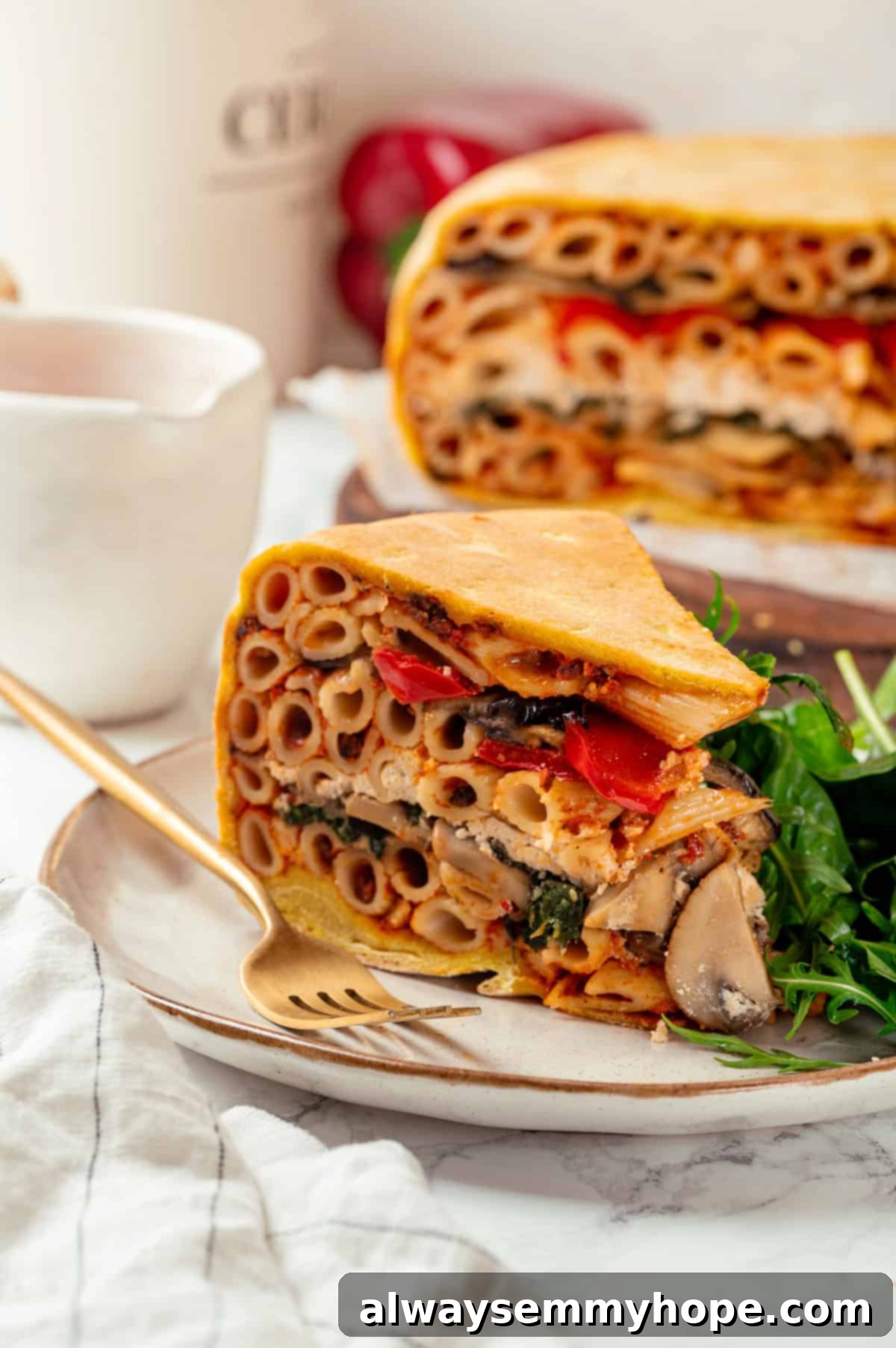 This vegan timpano recipe is perfect for the holidays! It’s loaded with pasta, veggies and plant-based cheese, all baked in a pastry crust. A delectable slice of vegan timpano on a white plate, showcasing its golden crust and richly layered filling, ready to be enjoyed.