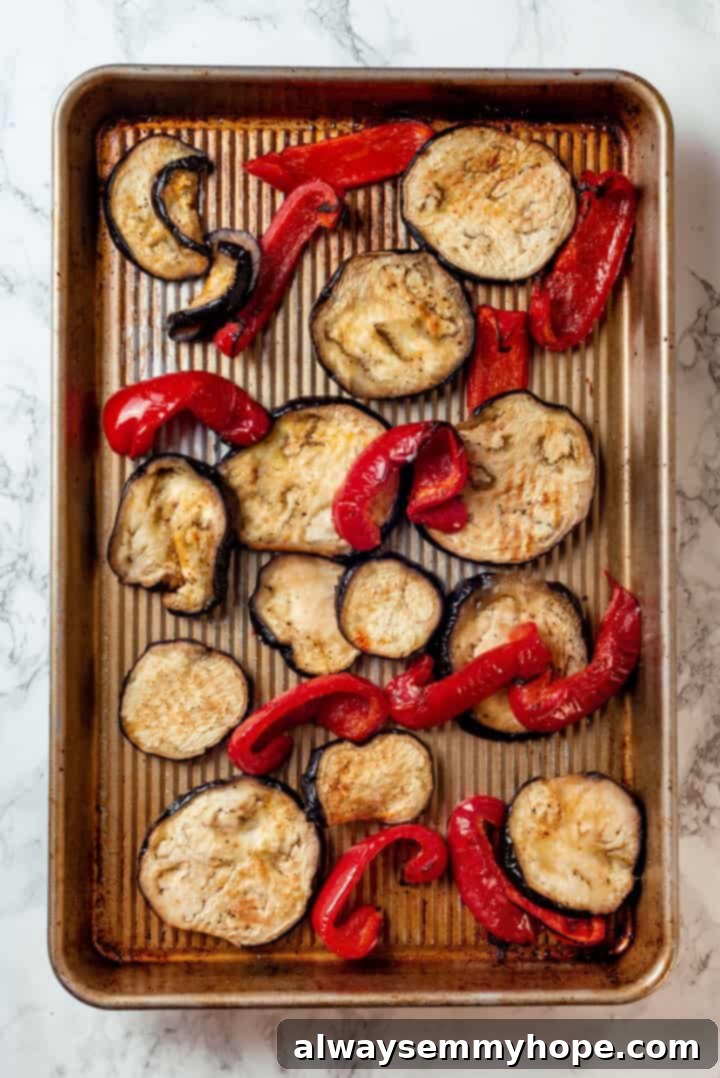 This vegan timpano recipe is perfect for the holidays! It’s loaded with pasta, veggies and plant-based cheese, all baked in a pastry crust. Sheet pan filled with sliced eggplant and red bell peppers, glistening with olive oil, salt, and pepper, just after roasting to tenderness.