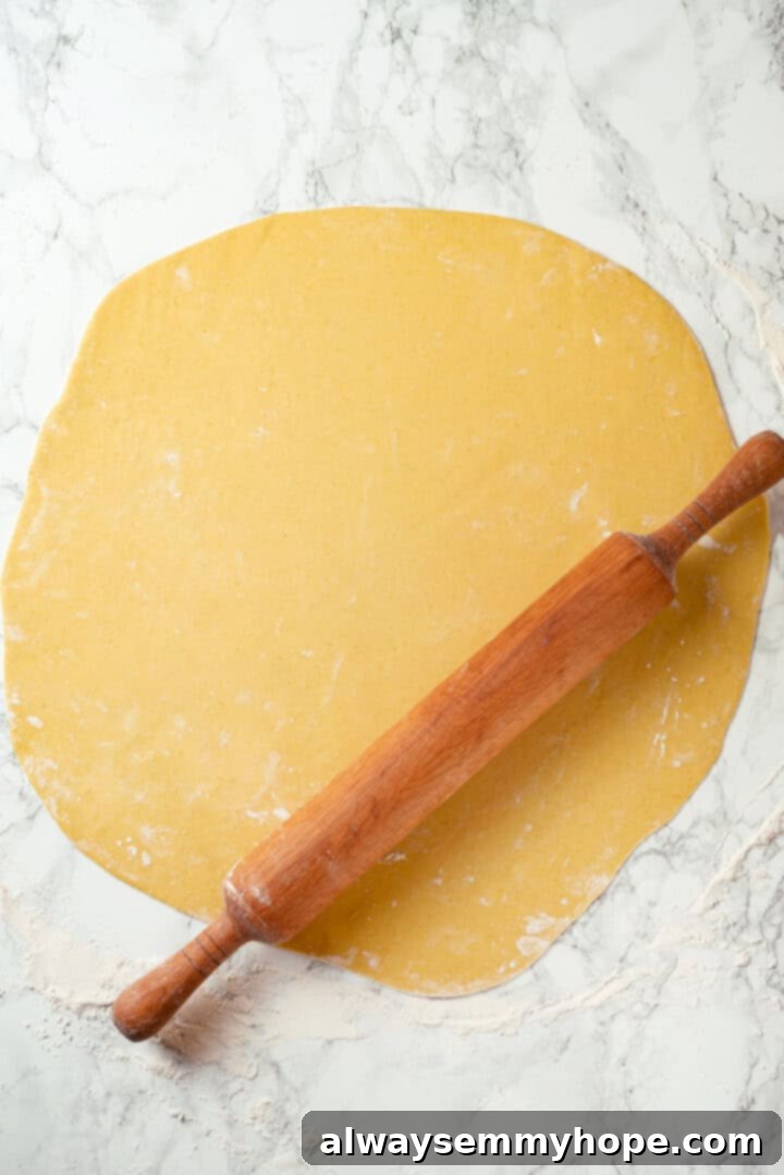 This vegan timpano recipe is perfect for the holidays! It’s loaded with pasta, veggies and plant-based cheese, all baked in a pastry crust. A rolling pin working a large circle of timpano dough on a lightly floured surface, ready to be placed in the Dutch oven.