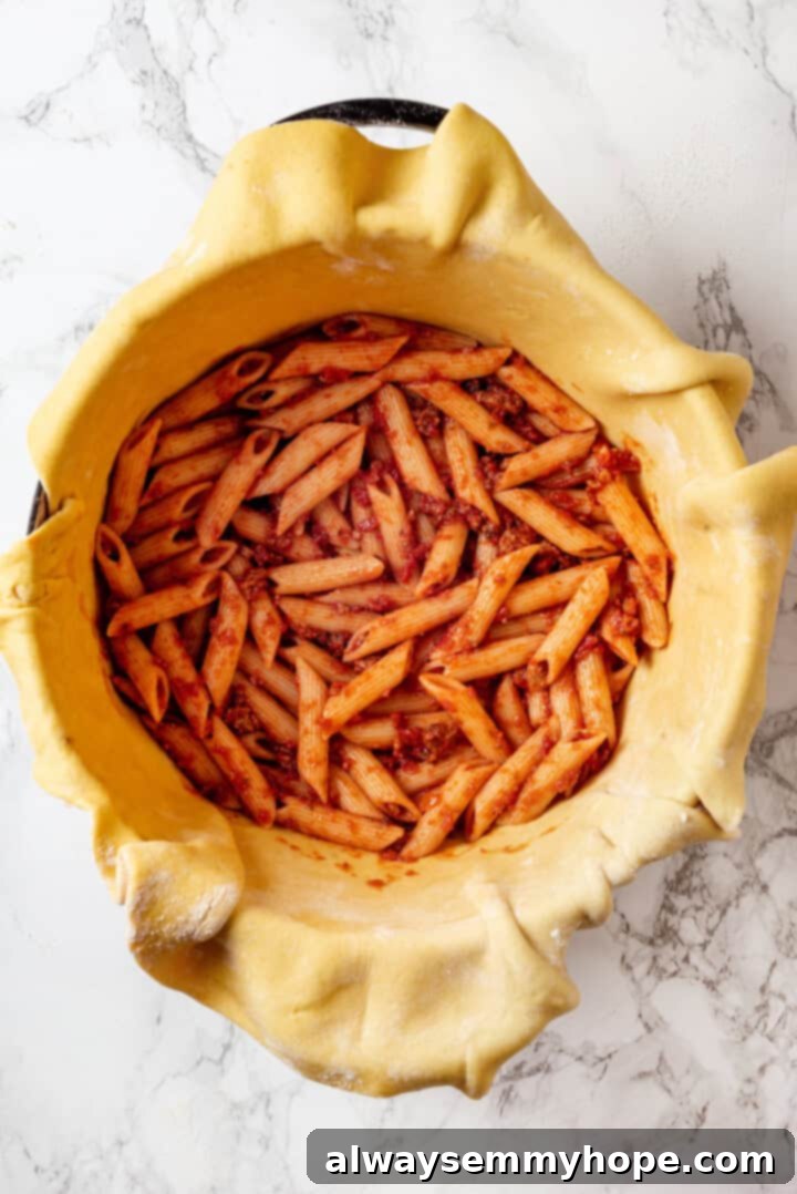 This vegan timpano recipe is perfect for the holidays! It’s loaded with pasta, veggies and plant-based cheese, all baked in a pastry crust. The first layer of pasta mixed with marinara sauce and vegan sausage, evenly spread at the base of the dough-lined Dutch oven for the timpano.