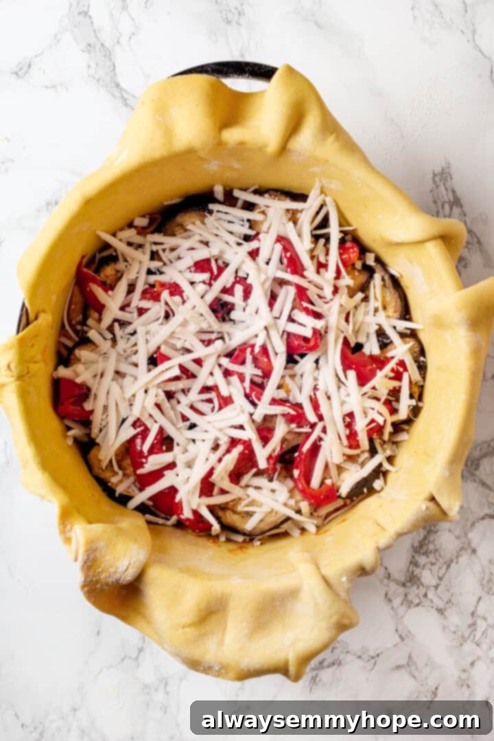 This vegan timpano recipe is perfect for the holidays! It’s loaded with pasta, veggies and plant-based cheese, all baked in a pastry crust. A generous layer of roasted eggplant and bell peppers topped with shredded vegan mozzarella cheese inside the timpano, ready for the next layer.