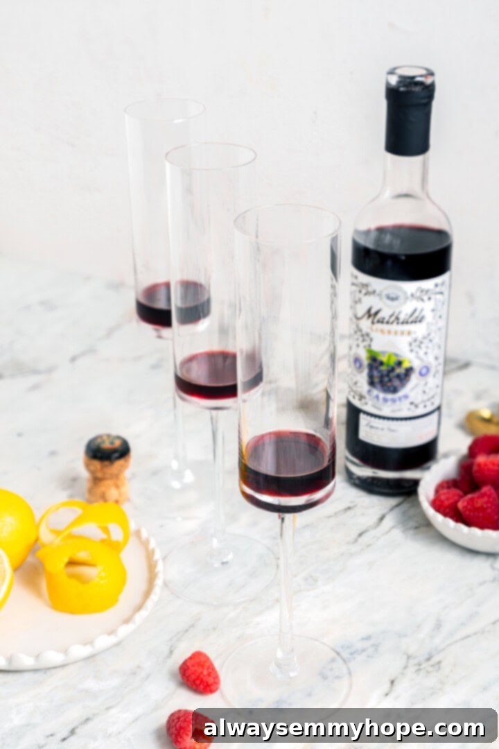 Three champagne flutes each containing a measure of deep red crème de cassis, ready for the sparkling wine.