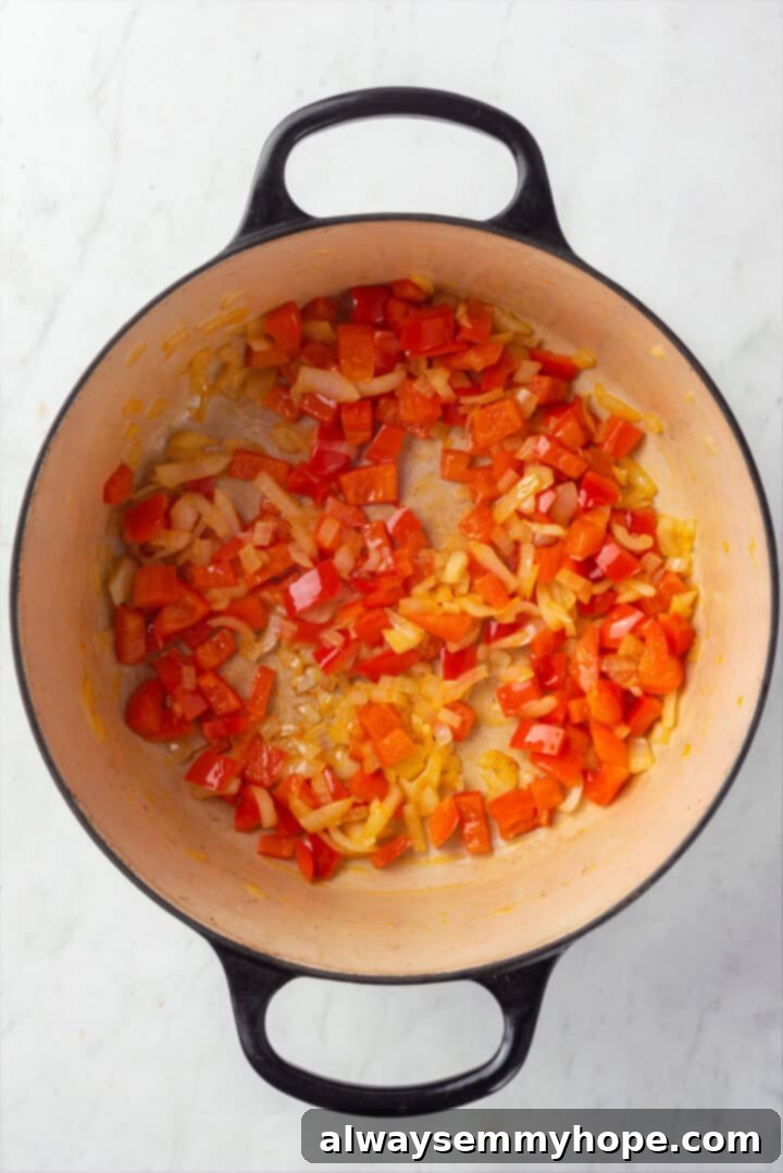 This vegan taco soup packs in a whole lot of flavour! With a zesty broth, lots of beans, and veggies, this soup is hearty and satisfying. Onions and red pepper cooking in Dutch oven