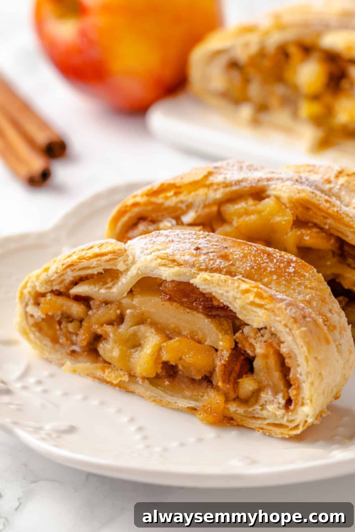 This easy apple strudel recipe wraps tender cinnamon-spiced apples in flaky puff pastry for a cozy treat. It's always a hit! Two slices of vegan apple strudel on plate, dusted with powdered sugar