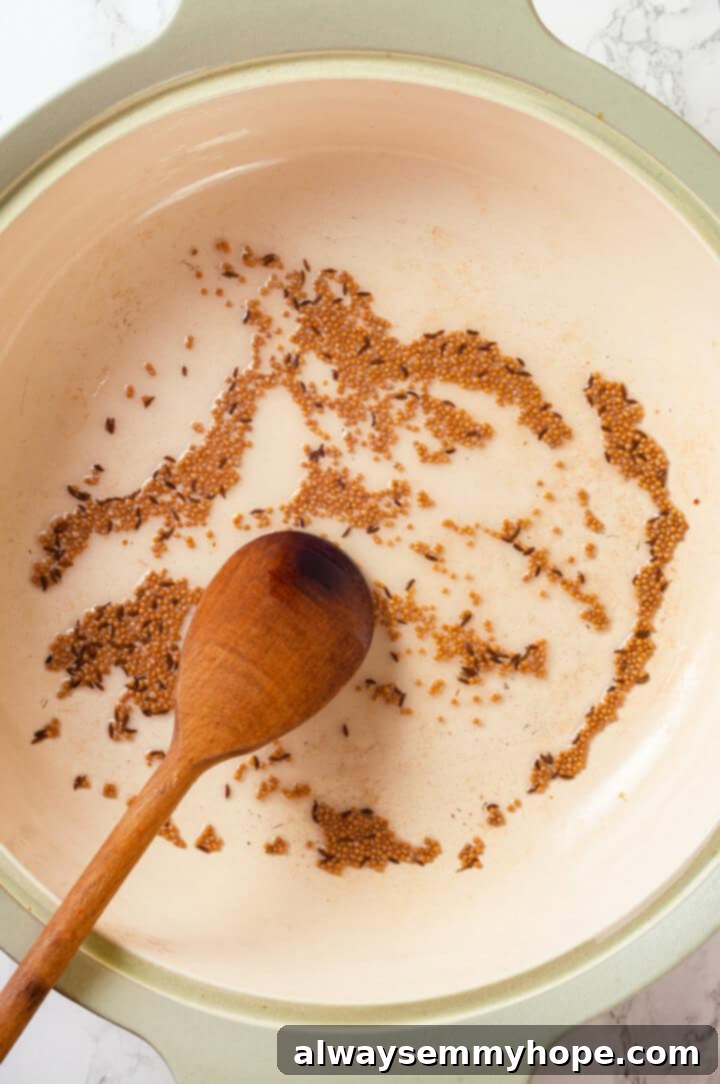 Tempering Spices: Cumin and Mustard Seeds Cumin and mustard seeds sizzling in hot oil in a large pan, just as they begin to pop and release their potent aromas, a key step in tempering.